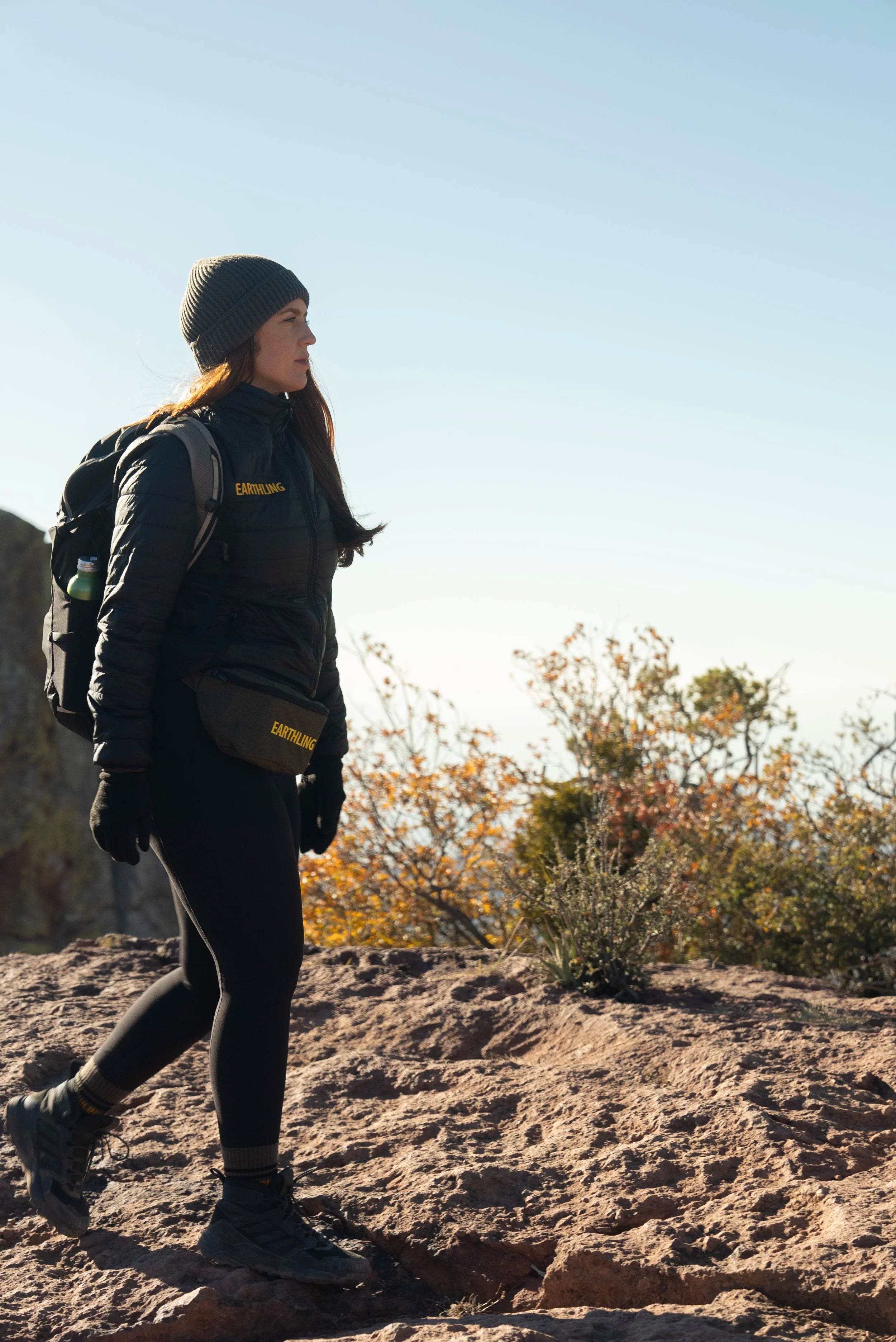 Hiker in black Earthling Outerwear layers with a pack on a desert trail