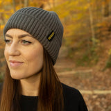 Dark gray Earthling knit beanie with the Earthling cuff tag, worn outdoors in autumn woods