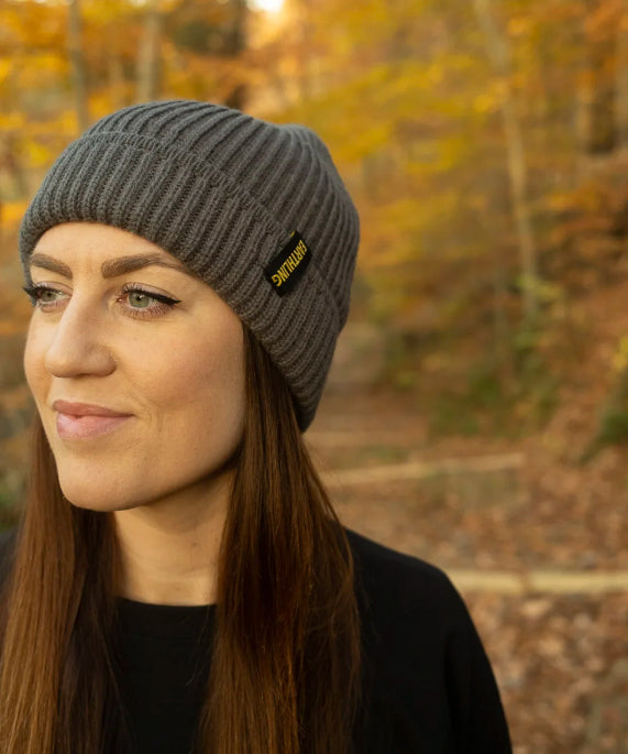 Dark gray Earthling knit beanie with the Earthling cuff tag, worn outdoors in autumn woods