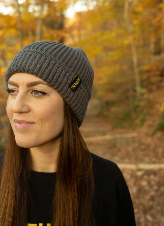 Dark gray Earthling knit beanie with the Earthling cuff tag, worn outdoors in autumn woods