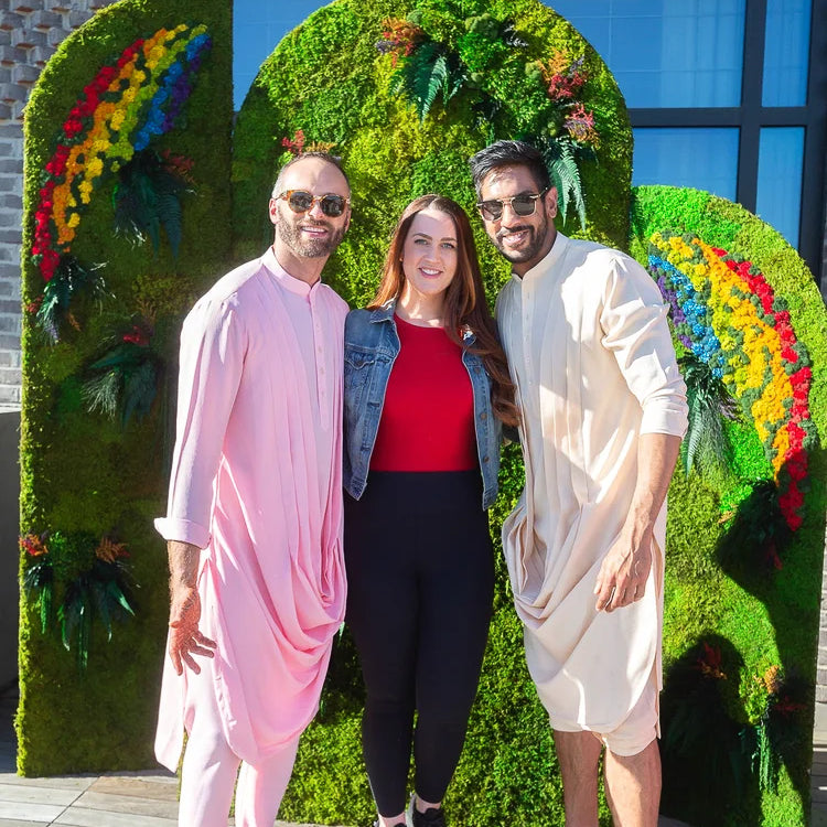 Amrit and Nicholas with a guest in front of a rainbow moss step and repeat wall