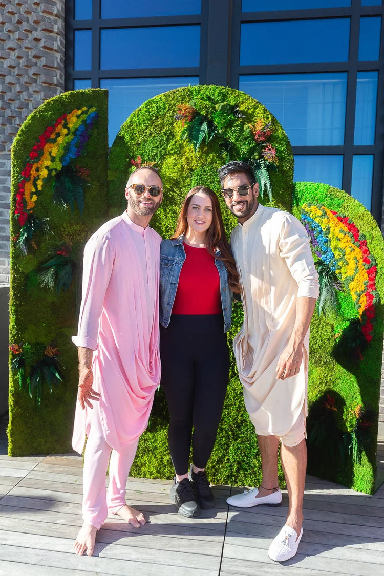 Amrit and Nicholas with a guest in front of a rainbow moss step and repeat wall