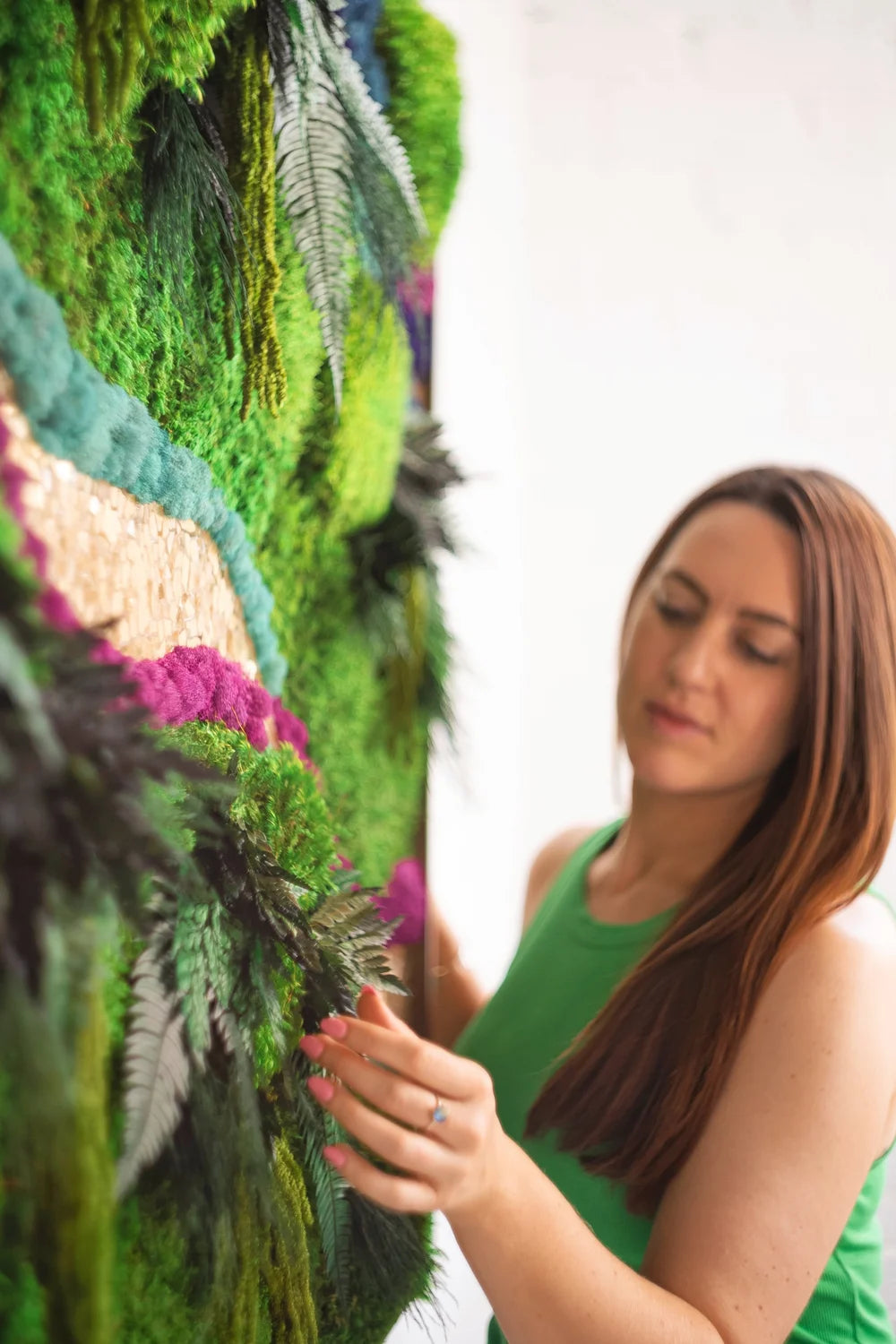 Woman standing in front of a preserved moss wall with ferns and flowers