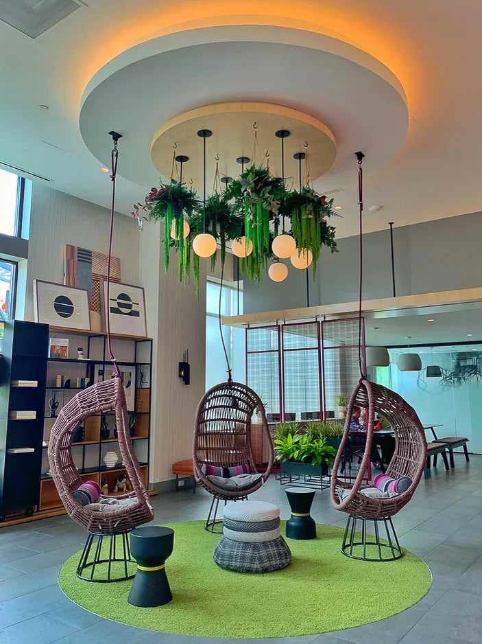 Suspended greenery chandelier and pendant lights over hanging rattan chairs in an office lounge
