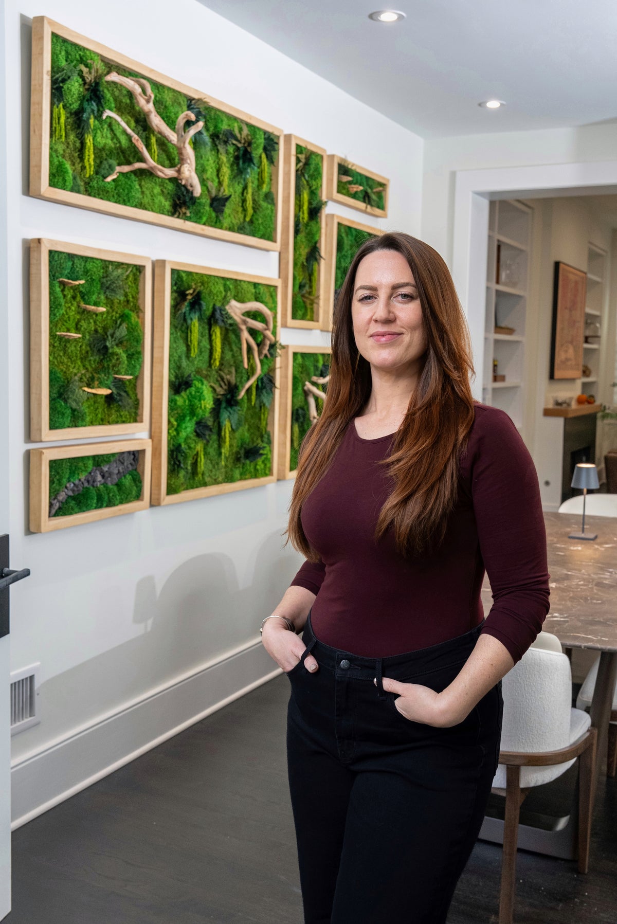 Kate Shooltz standing in front of a wall of framed preserved moss pieces in a client's home