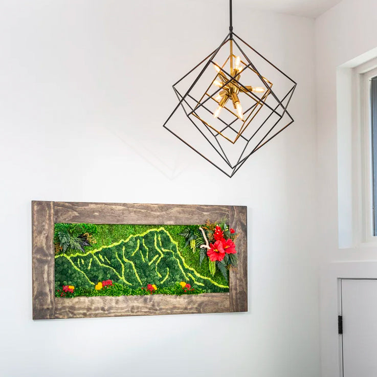 Horizontal barnwood framed moss piece with a pale winding trail and red blooms under a geometric chandelier