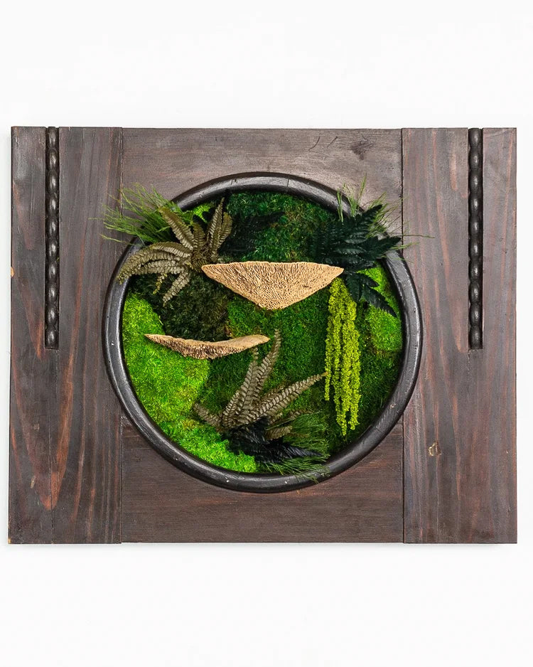 Preserved moss art inside a black metal ring on a dark reclaimed wood panel, with ferns and amaranthus