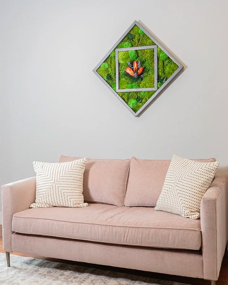 Square moss artwork hung on point in a silver frame with coral leaf forms, above a blush sofa