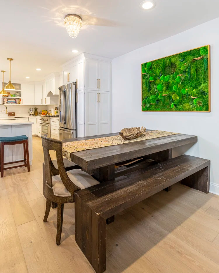 Gold framed moss artwork with round mushroom forms on a dining room wall above a reclaimed wood table and bench, wide view