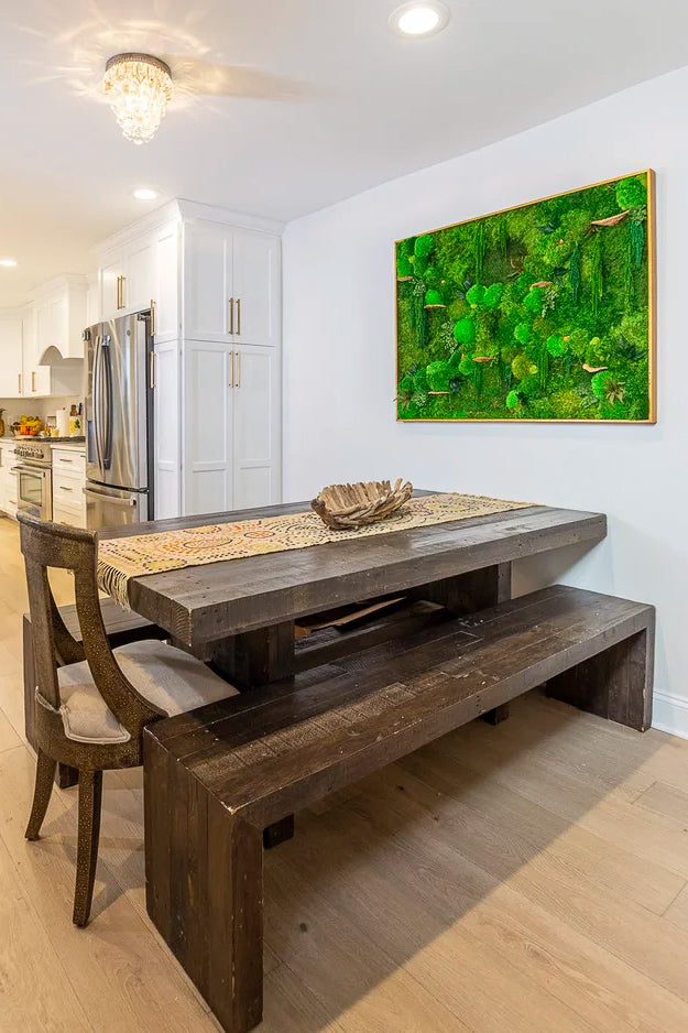 Gold framed moss artwork with round mushroom forms on a dining room wall above a reclaimed wood table and bench
