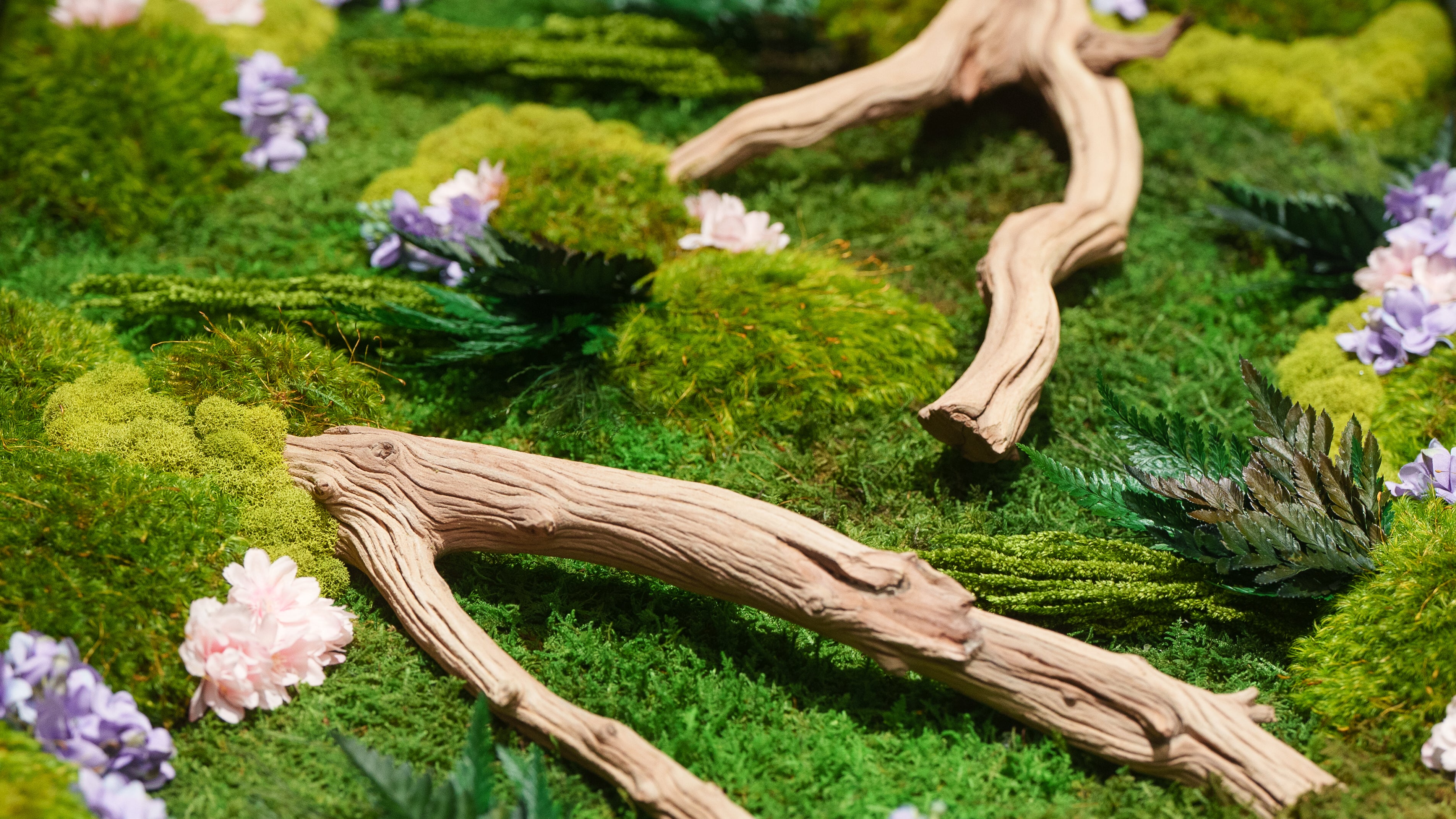 Close up of a preserved moss landscape with driftwood branches and pink and purple blossoms