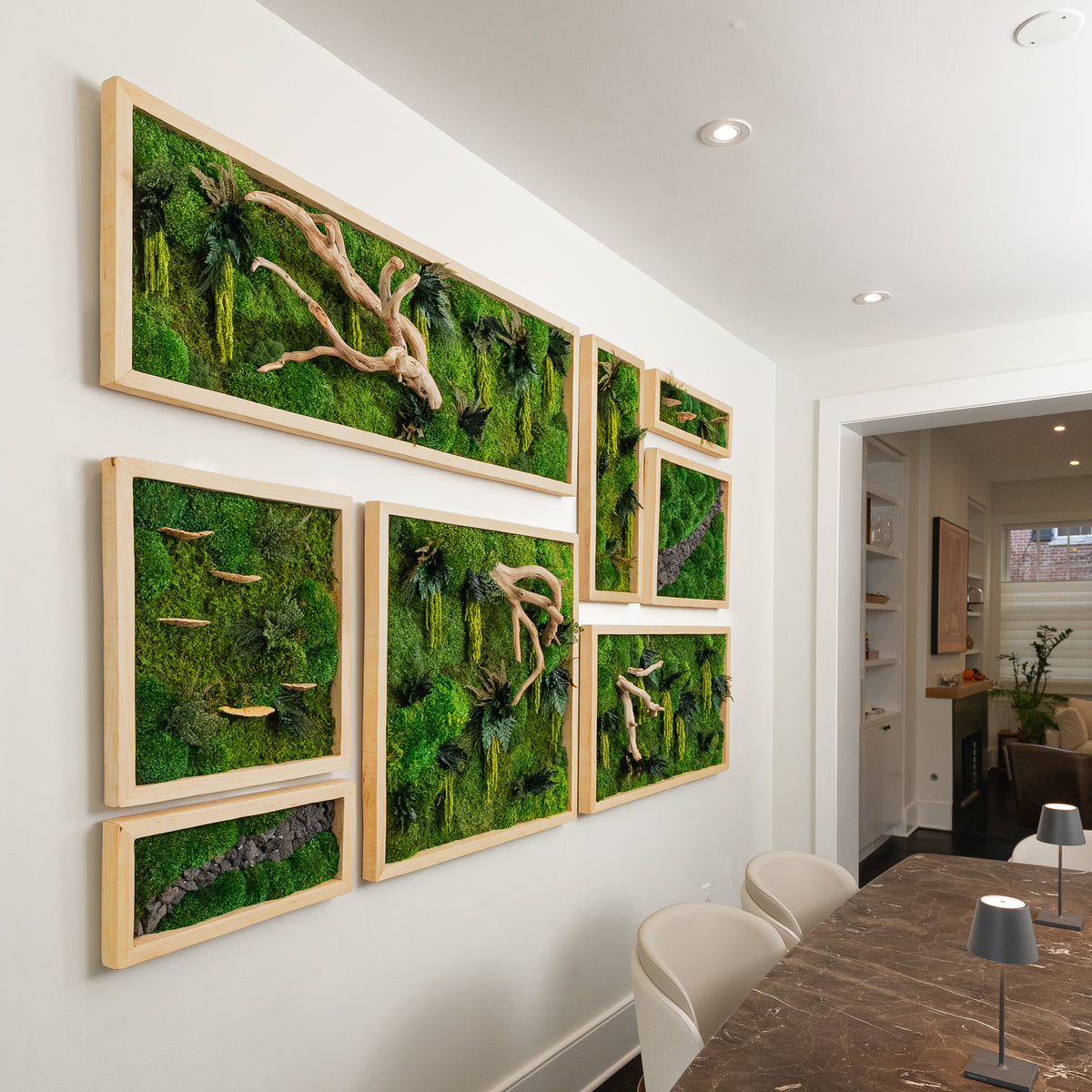 Cluster of light wood framed moss panels with driftwood branches filling a dining room wall