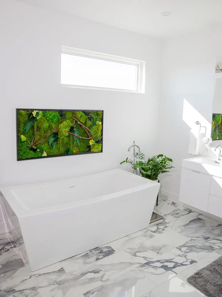 Horizontal moss panel in a dark frame above a freestanding tub in a white marble bathroom