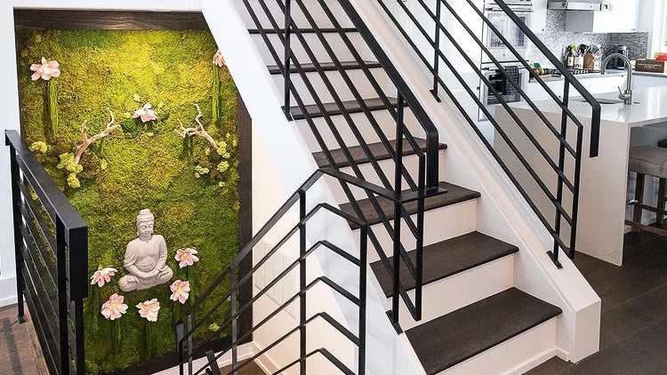 Moss panel with a stone Buddha and pale pink blossoms mounted on a stairwell wall beside a black railing