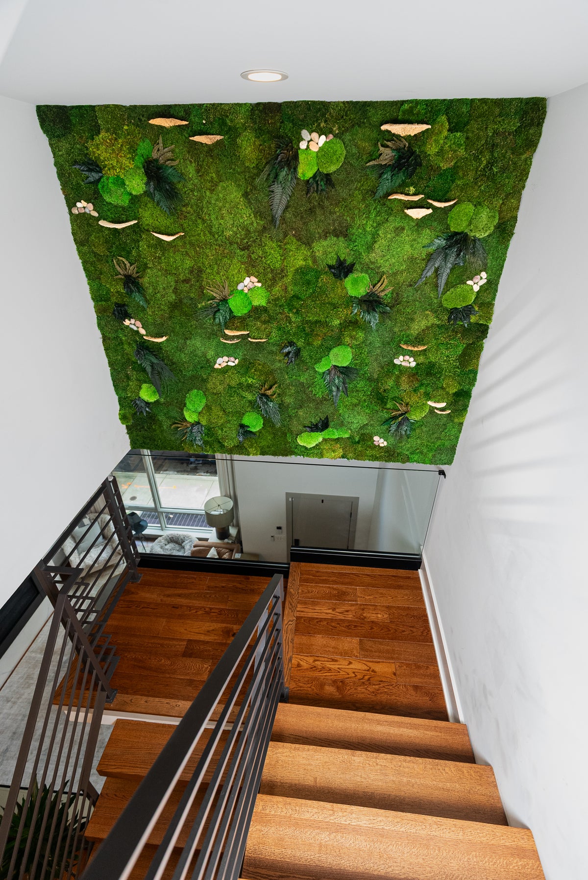 Full moss wall with mushroom caps and white blooms covering a stairwell, seen from the landing above