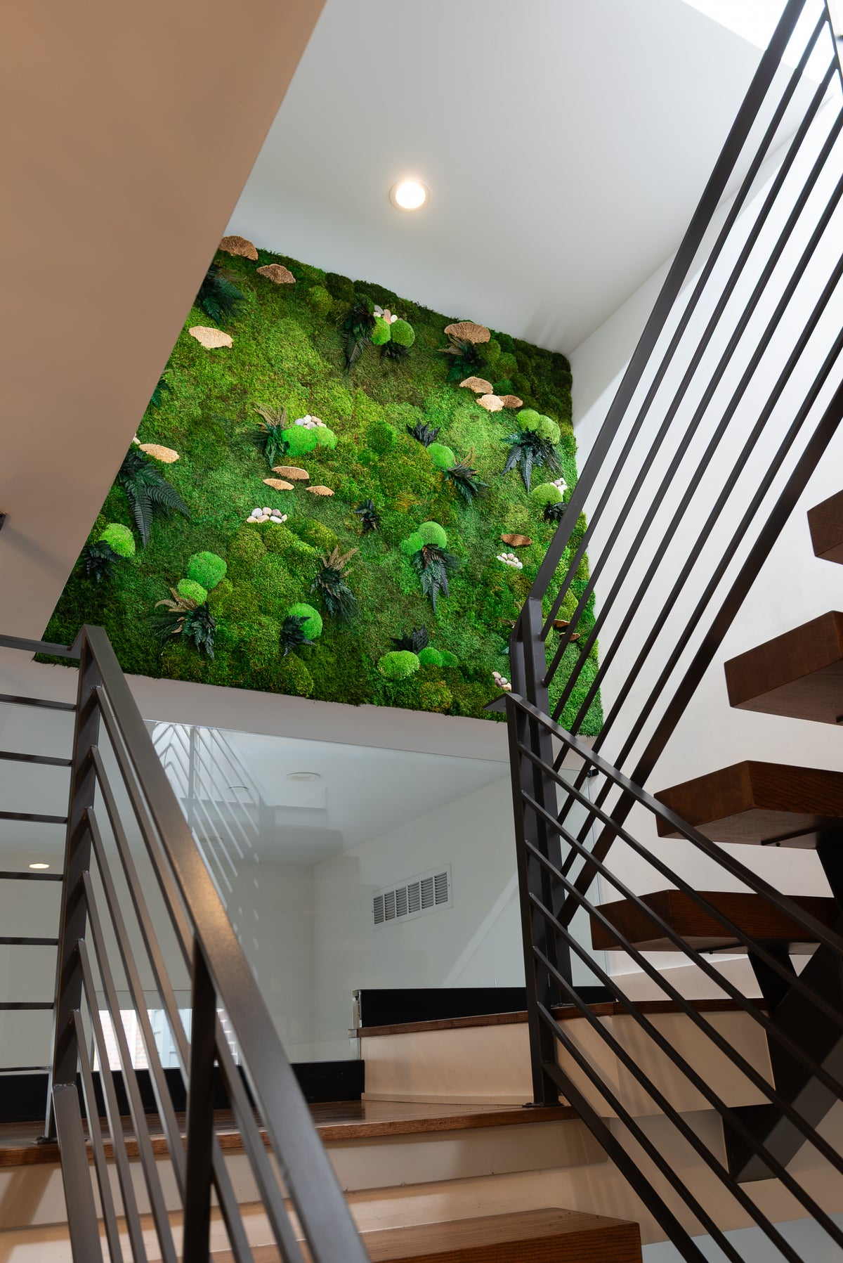 Preserved moss stairwell wall seen from below, with floating wood treads and a black metal railing