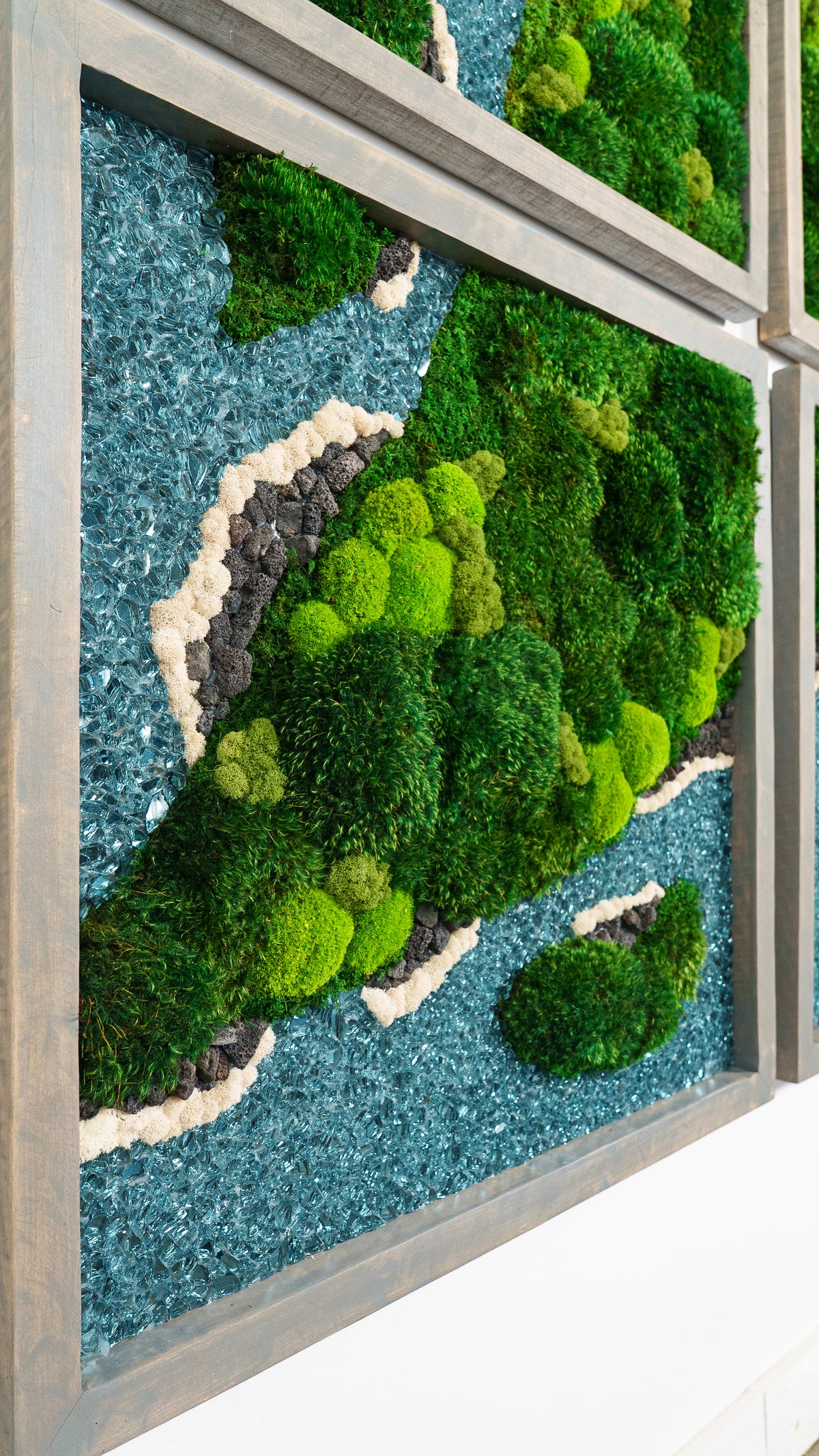 Framed moss panels with blue waterways, seen at an angle on a white wall